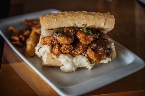 A hearty sandwich filled with fried chicken, gravy, and green onions, served with crispy fries on the side.