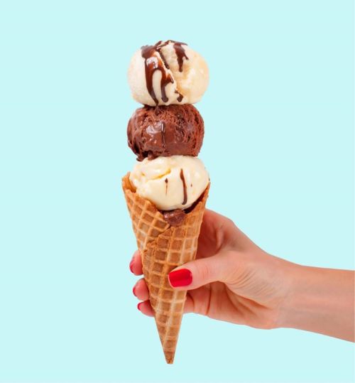 A hand holding a waffle cone with three scoops of ice cream: chocolate, vanilla, and a swirl of chocolate sauce.