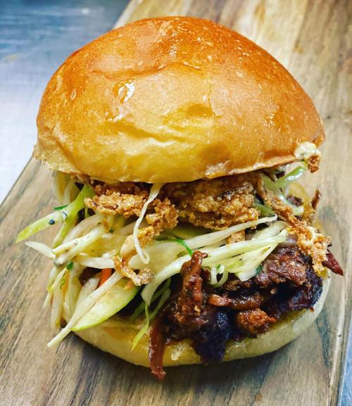 A delicious burger with crispy toppings and fresh slaw, served on a toasted bun on a wooden board.