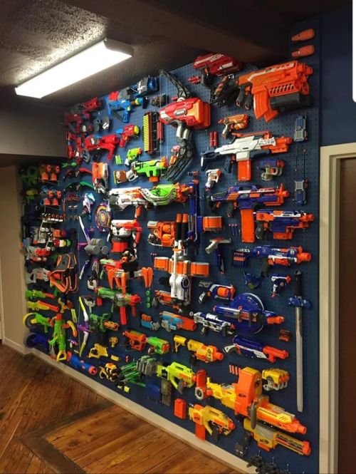 A colorful wall display filled with various toy blasters and Nerf guns organized on a pegboard.
