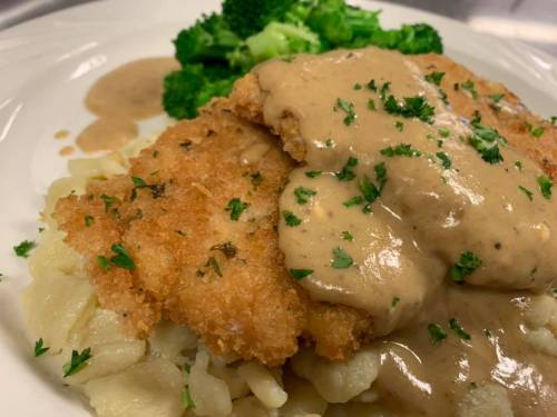 Crispy fried chicken on a bed of pasta, topped with creamy gravy and served with steamed broccoli.