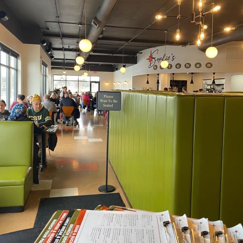 Interior of a busy restaurant with green booths, a waiting sign, and diners enjoying their meals.
