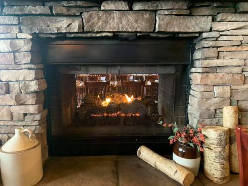 A cozy stone fireplace with a glowing fire, surrounded by logs and decorative items.