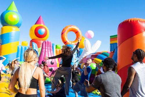 A lively scene at a colorful inflatable playground with people playing and enjoying a sunny day.