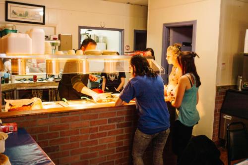 A group of people at a counter in a kitchen, interacting with a cook serving food. Warm, inviting atmosphere.