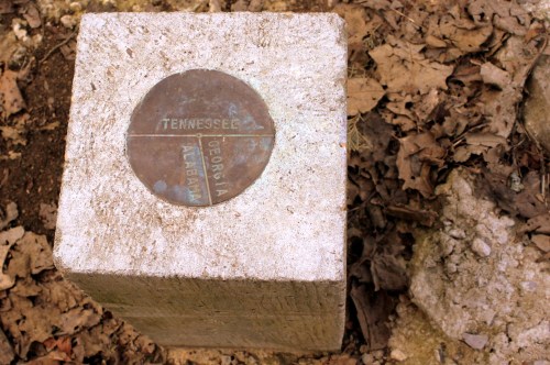 A concrete marker with a metal plate indicating the borders of Tennessee, Georgia, and Alabama, surrounded by leaves.