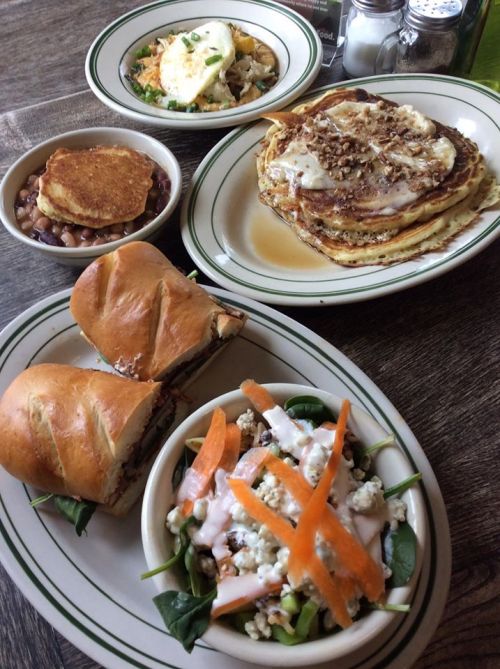 A table with a variety of dishes: pancakes with syrup, a sandwich, a salad, and a bowl of beans.