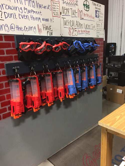 A wall display featuring red and blue laser tag guns, with safety instructions and pricing information in the background.