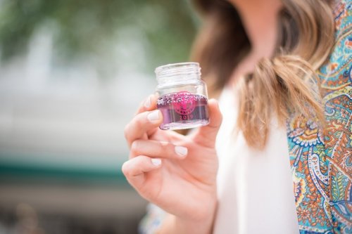 A person holds a small jar filled with purple liquid and glitter, wearing a colorful patterned top.