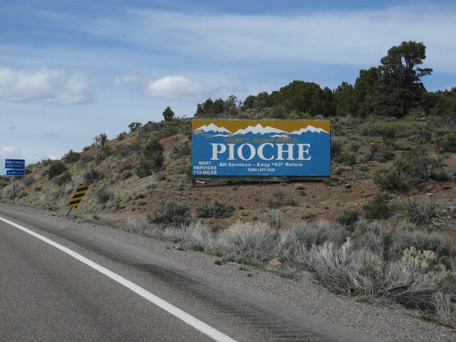 Sign for Pioche, Nevada, with mountains in the background, indicating next services and distance.