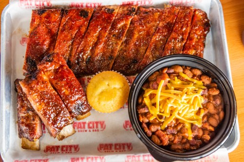 A platter of glazed ribs, cornbread muffin, and a bowl of chili topped with cheese, served at Fat City Brew & BBQ.