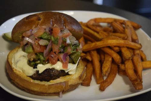 A juicy burger topped with fresh salsa and mayo, served with a side of crispy sweet potato fries.