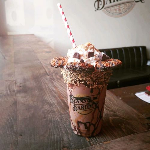 A decadent chocolate milkshake topped with whipped cream, cookies, and a red straw, served in a branded cup.