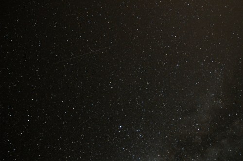 A starry night sky filled with countless stars and a faint streak of a meteor.