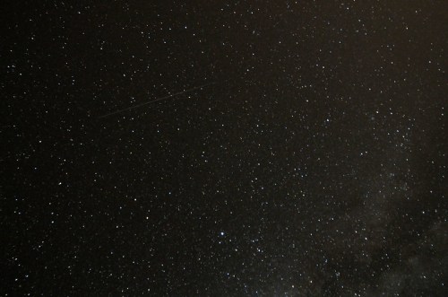 A starry night sky filled with countless stars and a faint streak of a meteor.