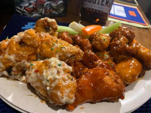 A plate of assorted chicken wings with different sauces, garnished with celery and a carrot stick.