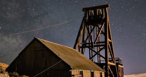 Abandoned mining structure illuminated at night, set against a starry sky and distant glowing lights.