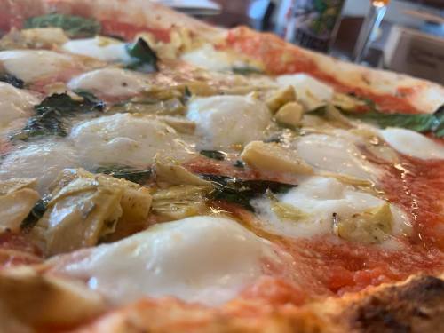 Close-up of a pizza topped with mozzarella, artichokes, and fresh basil on a tomato sauce base.