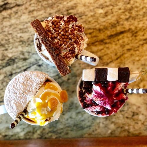 Three colorful desserts in cups: one topped with whipped cream and chocolate, another with fruit, and a third with berries.
