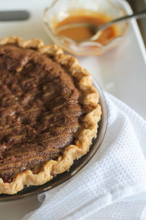 A freshly baked pie with a golden crust, placed on a white cloth, alongside a small bowl of caramel sauce.