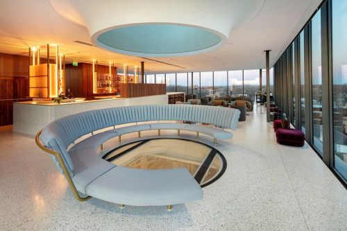 Modern lounge with a curved gray sofa, bar area, and large windows offering a city view. Elegant and spacious design.