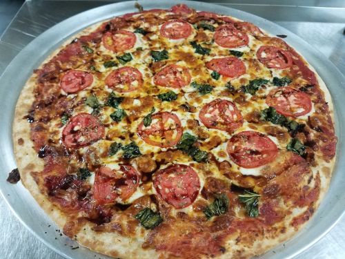 A freshly baked pizza topped with sliced tomatoes, cheese, and leafy greens on a golden crust.