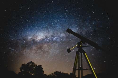 A telescope silhouetted against a starry night sky filled with the Milky Way.