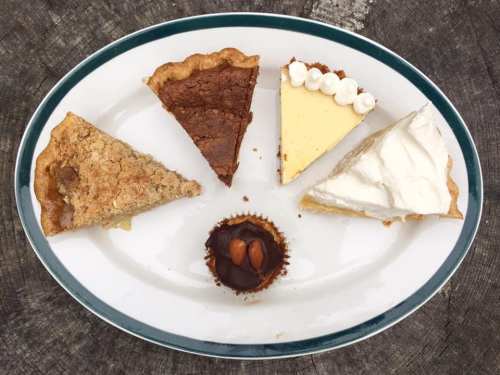 A platter with five slices of different pies and a small chocolate dessert topped with an almond.