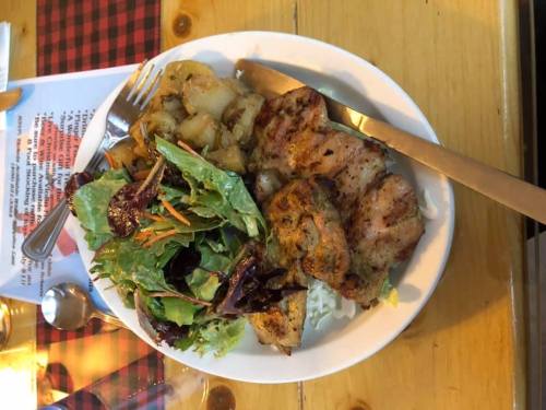 A plate of grilled chicken with rice, sautéed vegetables, and a fresh salad on a wooden table.