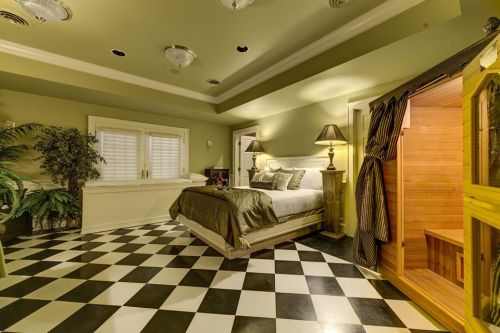 A stylish bedroom with a checkered floor, a bed, lamps, and a sauna in the corner, featuring green walls and elegant decor.