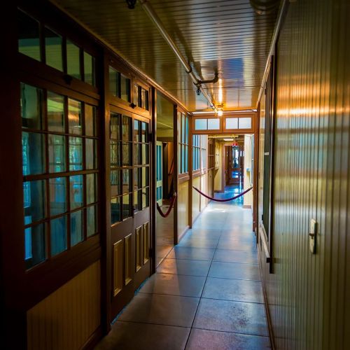 A long, well-lit hallway with wooden doors and windows, featuring a smooth floor and a red rope barrier.