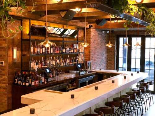 A stylish bar with a marble countertop, wooden beams, and a well-stocked shelf of various spirits and wines.