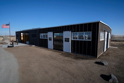 A modern black building with white doors, set against a clear blue sky and an American flag nearby.