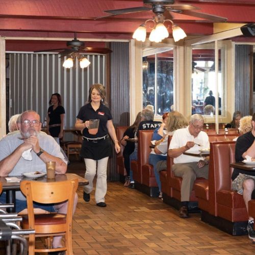 A busy restaurant interior with diners at booths and a server carrying drinks. Warm, inviting atmosphere.