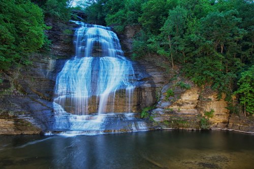 A serene waterfall cascading down rocky cliffs, surrounded by lush green trees and reflecting in a calm pool below.