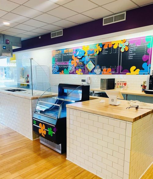 Brightly colored ice cream shop interior with a service counter, display freezer, and chalkboard menu on the wall.