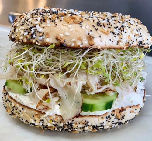 A bagel sandwich with poppy and sesame seeds, filled with sprouts, cucumber, and shredded chicken.