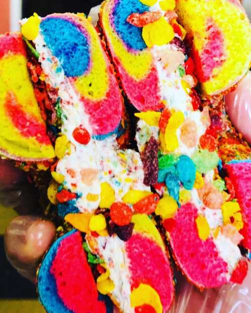 A colorful, layered dessert with vibrant pink, yellow, and blue hues, filled with cream and topped with candy pieces.