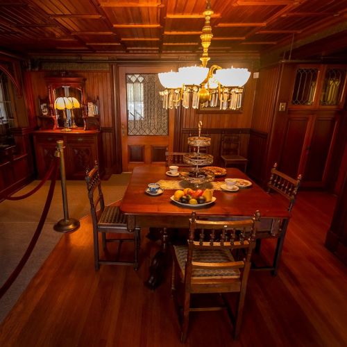 A warmly lit dining room featuring a wooden table set with dishes, a tiered stand, and elegant chandeliers.
