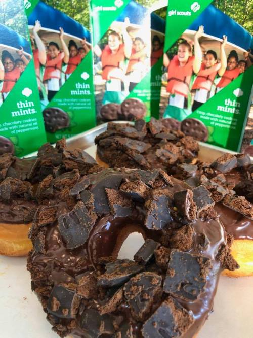 Chocolate donuts topped with Thin Mints cookies, with boxes of Thin Mints in the background.