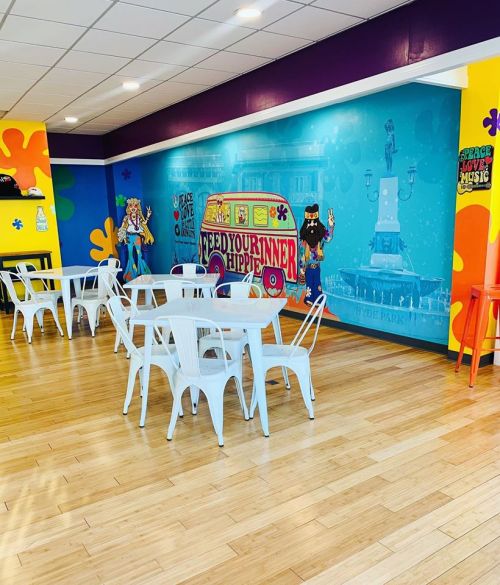 Brightly colored cafe interior with white tables and chairs, featuring a vibrant mural and playful decor.