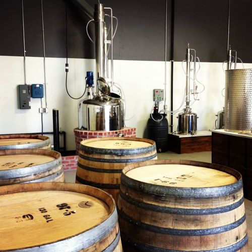 Interior of a distillery featuring wooden barrels and distillation equipment.