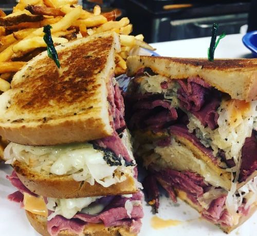 A stacked sandwich with layers of pastrami and sauerkraut, served with a side of crispy fries.