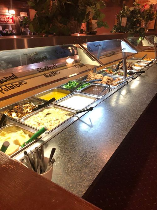 A buffet with various food options, including vegetables, pasta, and sauces, displayed in metal trays.