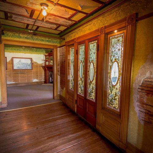 Interior view of a vintage hallway featuring ornate wooden doors with stained glass and intricate wall details.
