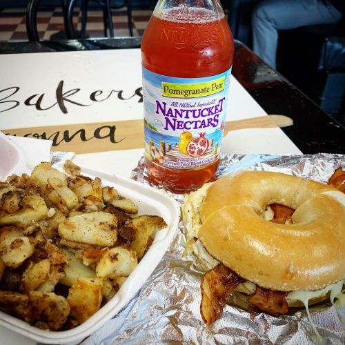 A bagel sandwich with chicken and coleslaw, served with seasoned potatoes and a bottle of pomegranate pear drink.