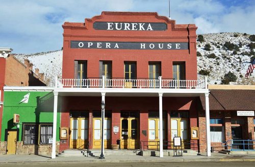 Historic Eureka Opera House with a red facade, white trim, and snow-capped mountains in the background.