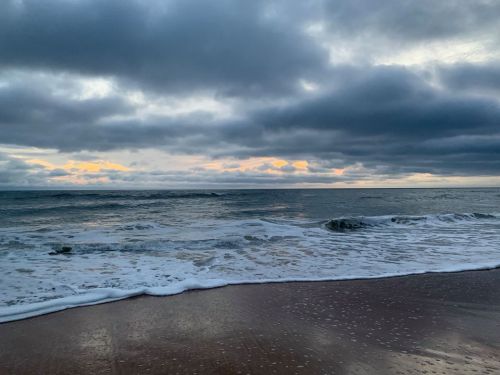 A serene beach scene with gentle waves, cloudy skies, and a hint of sunset on the horizon.