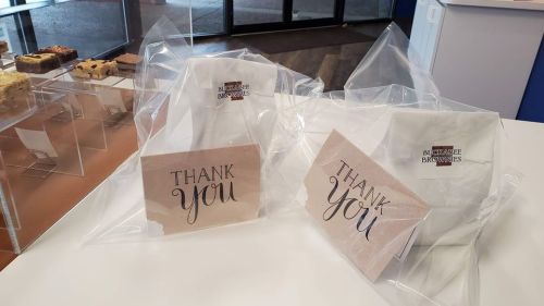 Two packages of brownies wrapped in clear plastic, each with a "Thank You" card displayed on a table.