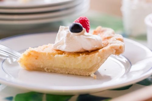 A slice of pie topped with whipped cream and berries, served on a white plate with a fork beside it.